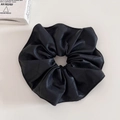 Vue détaillée d'un chouchou en similicuir noir matelassé sur un fond beige neutre - Noir