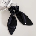 Detail of black satin bow scrunchie with white pearl accents on elegant white surface - Black