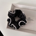 Dettaglio dell'elastico scrunchie in raso nero con bordi bianchi ed etichetta LUCY - Stile con Bordo Nero