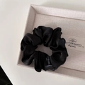 Dettaglio di scrunchie in raso nero con etichetta posizionato su vassoio beige - Nero Base