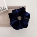 Detail of dark blue velvet scrunchie with brand woven label on elegant beige tray - Navy Blue