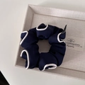 Detail of navy blue oversized scrunchie with white satin edge on a beige linen tray - Navy Blue With White Piping