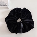 Detailed view of black velvet scrunchie texture with white printed brand label - Black