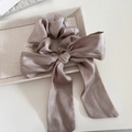 Detail eines champagnerfarbenen Satin-Haargummis mit Schleife auf einem beigen Display - Beige