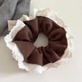Detailed close-up of dark brown ribbed fabric scrunchie with white lace floral trim - Brown