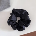 Close-up of black satin scrunchie featuring high-gloss texture and white brand label - Large / Black