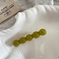 Dettaglio di perle in resina verde su un fermaglio dorato posto in un piatto a conchiglia - Stile Turchese Verde Traslucido