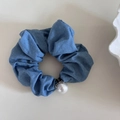 Dettaglio di elastico in denim blu con grande perla e trama su sfondo beige neutro - Azzurro