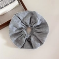 Close-up of a grey fabric scrunchie with delicate pom-pom trim on a minimalist white surface - Gray