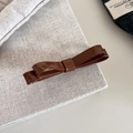 Dettaglio di un fermaglio per capelli a doppio fiocco in pelle marrone lucida su borsa - Marrone