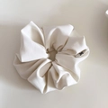 Macro view of textured cream scrunchie fabric and white tag with bow icon detail - White
