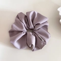 Detail view of a thick purple fabric scrunchie with fine texture and branded label - Purple