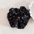 Detailed macro view of black satin floral scrunchie with a logo label and white flowers - Black