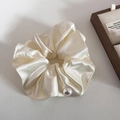 Detail shot of a cream satin scrunchie with a large pearl accent on a textured surface - Beige