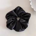Detail view of a black satin scrunchie with glossy texture on a light beige background - Black
