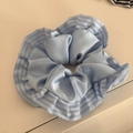 Close-up of light blue satin scrunchie featuring elegant ruffled edges with stripe pattern - Blue