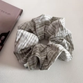 Dettaglio di scrunchie a quadri verdi con bordo in pizzo ed etichetta tessuta su sfondo grigio - Verde