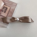 Détail de la barrette à nœud en satin champagne avec perle et étiquette dorée - Champagne