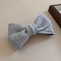 Dettaglio del fermaglio a fiocco in feltro grigio con targhetta in metallo dorato - Marmo Grigio