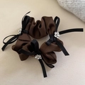 Detail eines Satin-Haargummis mit glitzernden Strass-Schleifen und brauner Stoffstruktur - Braun