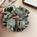 Detailed view of sage green satin scrunchie with elegant ruffled texture for ponytail - Green