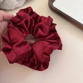 Détail d'un chouchou en satin bordeaux montrant la texture brillante et l'élasticité - Rouge