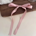 Detailed view of elegant pink satin bow hair clip with long flowing ribbons on wood base - Pink