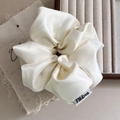 Detail of oversized cream satin scrunchie showing glossy texture and branded fabric tag - White