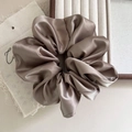Detail of oversized champagne satin scrunchie on wooden tray and linen cloth decor - Brown