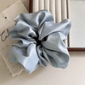Macro shot of oversized light blue satin scrunchie with soft fabric pleats on a tray - Blue