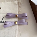 Detail view of two lavender ribbon bow hair clips with gold metal centers on linen - Light Purple