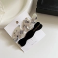 Dettaglio di due fermagli vintage in acetato marmorizzato e nero su carta bianca - Nero