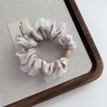 Détail d'un chouchou en satin beige avec dentelle blanche et perle bois sur plateau - Gris Beige