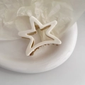 Dettaglio molletta a stella bianca opaca con molla dorata su un piatto in ceramica bianca - Bianco Sporco