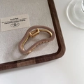 Detail of a brown acetate shark hair claw clip with golden metal frame on a wooden tray - Light Coffee