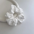 Detailed macro view of white pleated fabric scrunchie with brand logo label on ceramic plate - White