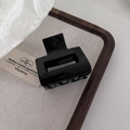 Detailed close-up of a glossy black acetate hair claw clip on a minimalist wooden tray - Black