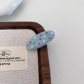Détail d'une petite barrette en résine bleu clair à pois colorés sur un plateau en bois - Pince Ovale Bleue