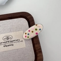 Close-up of an oval cream hair clip with colorful rainbow polka dots on a wooden tray - White Oval Hair Clip