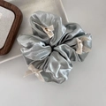 Dettaglio scrunchie metallico argento con tre fiocchi di nastro crema su vassoio ceramica - Verde
