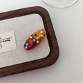 Amber resin oval hair clip with colorful polka dots on a wooden display tray - Brown