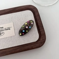 Detailed macro view of an oval tortoiseshell hair clip with colorful polka dots on wood - Black