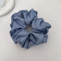 Detail view of dusty blue satin scrunchie showing glossy pleated silk fabric texture - Blue