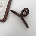 Close-up of a translucent brown hair claw clip with a modern twisted design on a white surface - Crossed / Dark Amber Brown