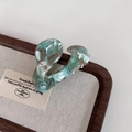 Detailed macro view of an acetic acid hair claw clip with green marble texture and gold script - Green