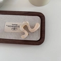 Eleganter cremefarbener Perlen-Haarclip mit S-förmiger Welle auf einem Holztablett - Champagner