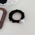Dettaglio di un elastico per capelli nero con una grande perla bianca su fondo bianco crema - Bianco