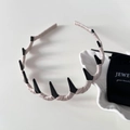 Détail d'un serre-tête en satin rose avec des pointes punk noires sur un bureau blanc - Blanc Cassé