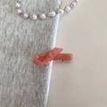 Detail of coral pink bow hair clip with gold logo on soft grey knit fabric - Pink