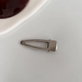 Dettaglio di un fermaglio per capelli triangolare in metallo argento con denti antiscivolo - Corto Vuoto